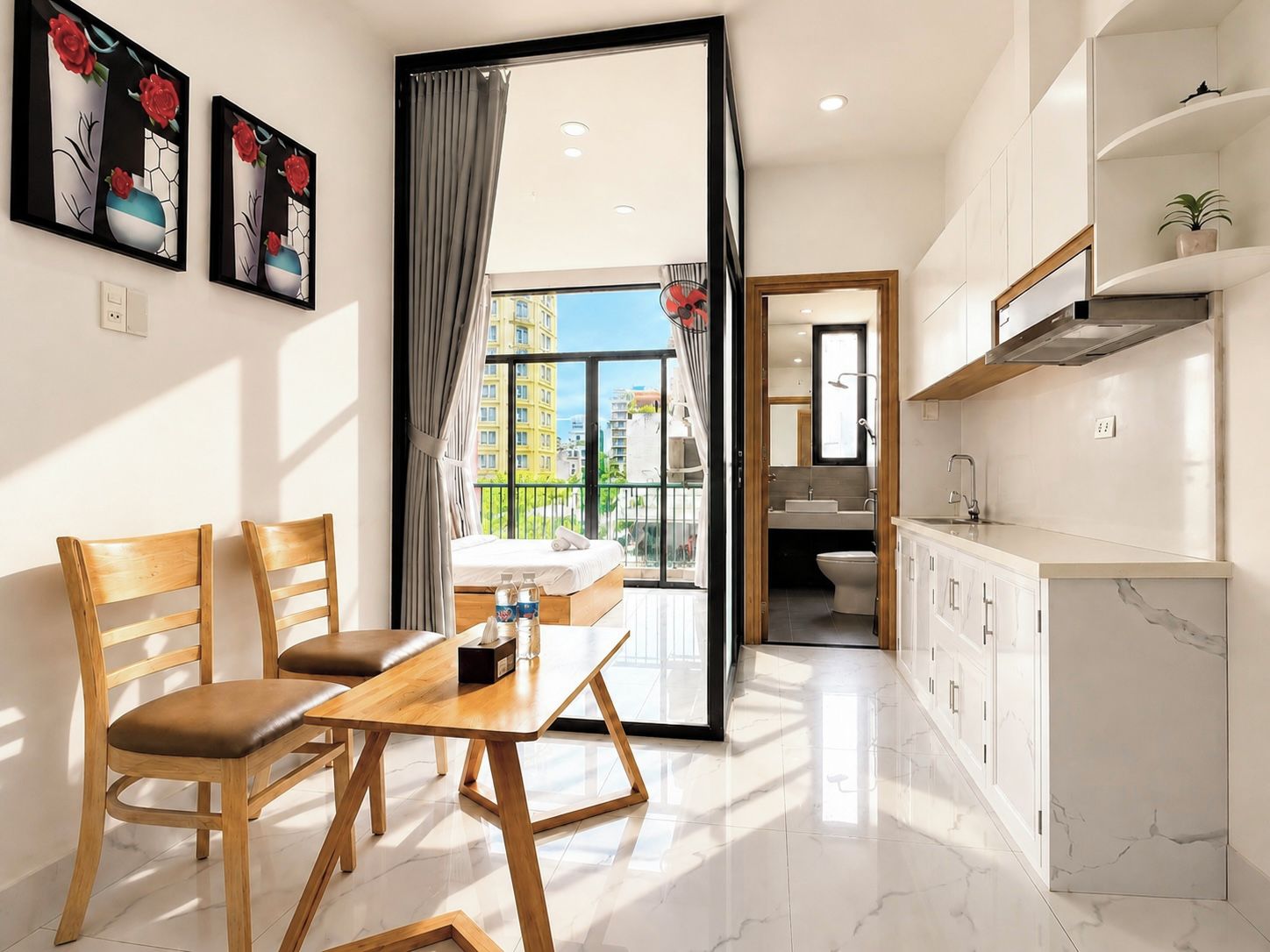 A modern hotel room with a dining area, a balcony with a view, and a separate bathroom.