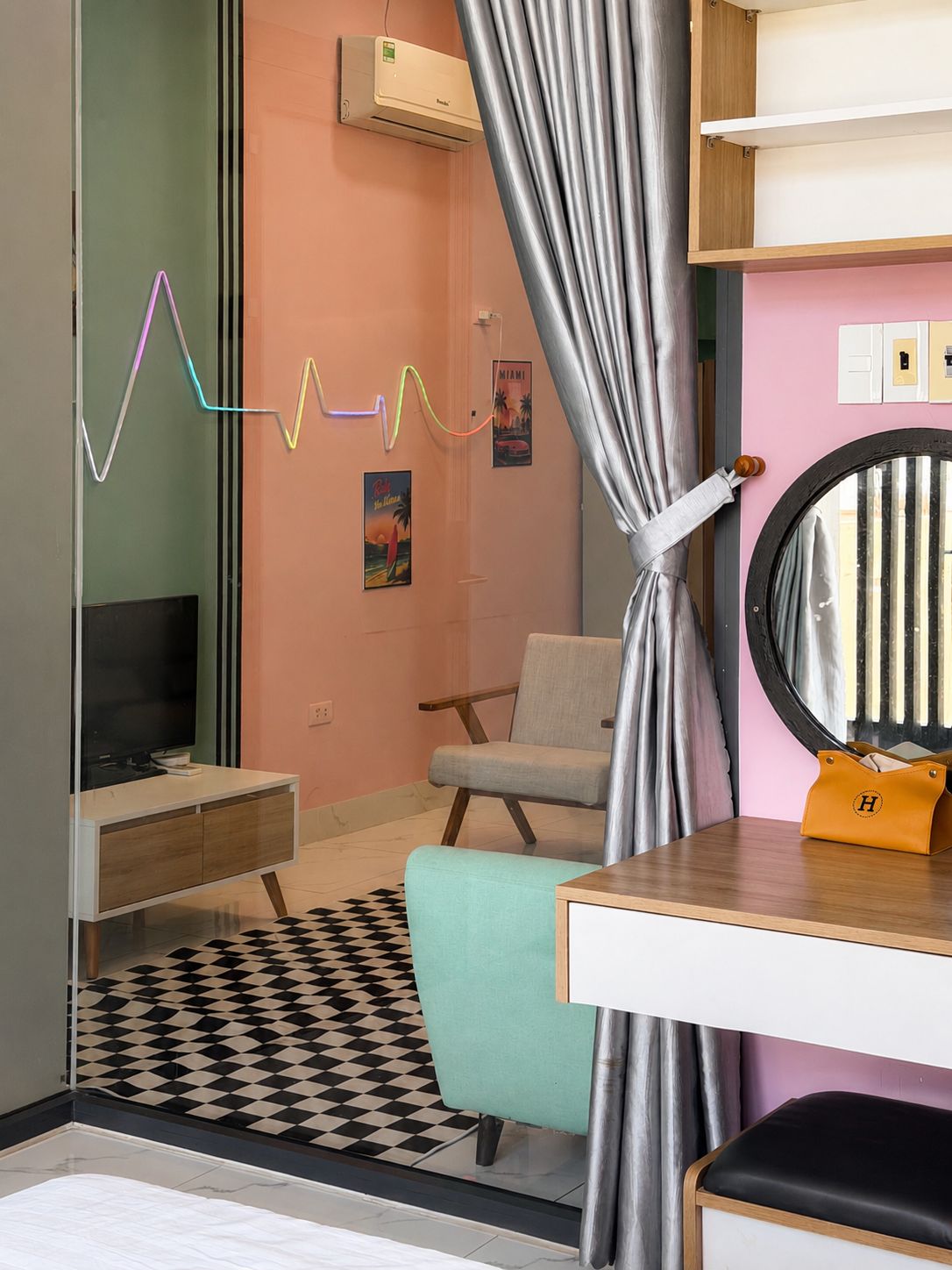 Quarto com televisão, uma cadeira, mesa com espelho e tapete estampado.