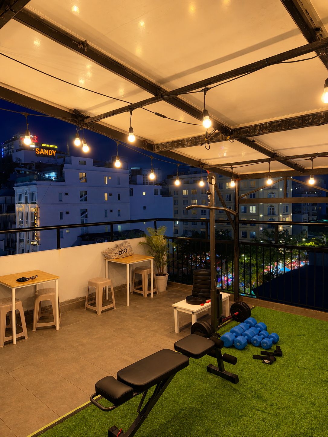 An outdoor workout area with exercise equipment, a table, and chairs, overlooking a cityscape at night.