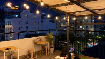 An outdoor workout area with exercise equipment, a table, and chairs, overlooking a cityscape at night.