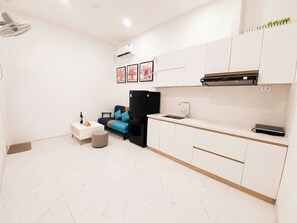 Cozinha compacta com armários brancos, geladeira preta, bancada branca e pia pequena.