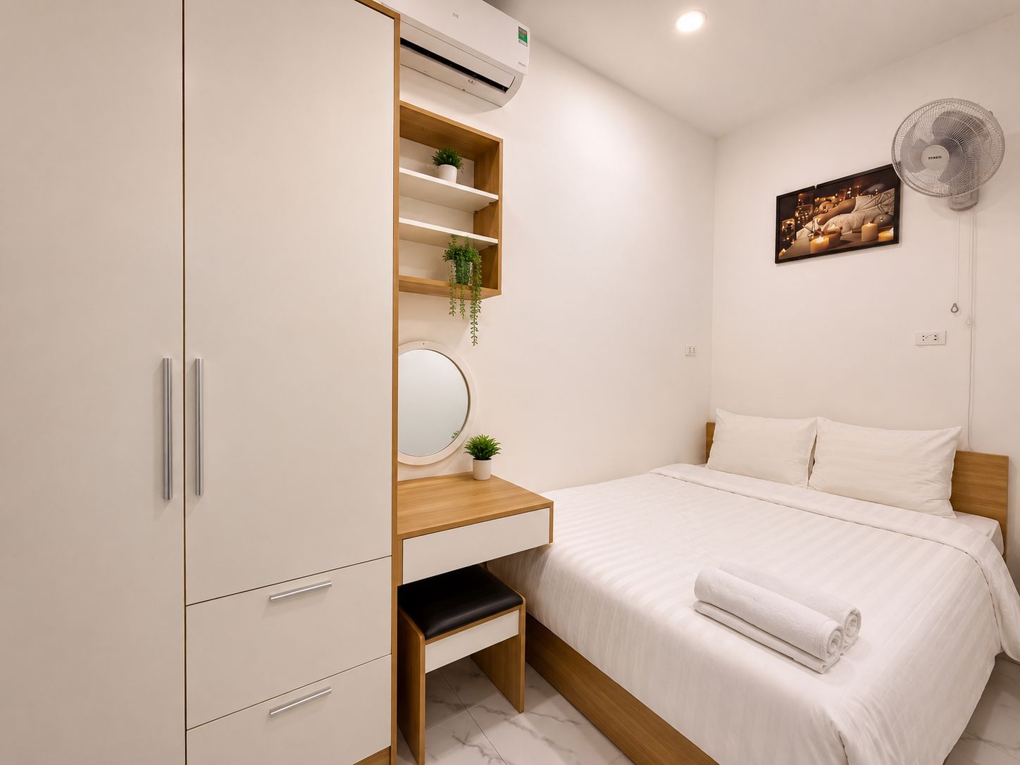 Quarto com cama, mesa de cabeceira, espelho, guarda-roupa e ventoinha fixada na parede.