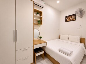 Quarto com cama, mesa de cabeceira, espelho, guarda-roupa e ventoinha fixada na parede.