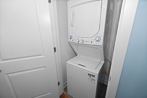 A compact laundry room with a washer and dryer, a door, and a small window. - Chicago 3BR Oasis Near Downtown & United Center (Chicago)