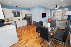 A modern kitchen with white cabinets, a stainless steel refrigerator, and a dining area with black chairs and a glass table. - Chicago 3BR Oasis Near Downtown & United Center (Chicago)