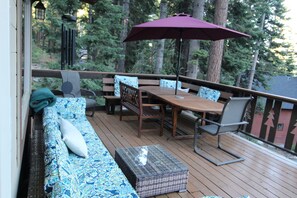 A wooden deck with a table and chairs, a cushioned bench, and a large umbrella. - Unique 3-bedroom home in charming Carnelian Bay-North Lake Tahoe, CA (Carnelian Bay)