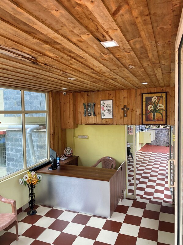 A reception area with a checkered floor, wooden ceiling, a reception desk, a clock, and a wall with a framed quote.