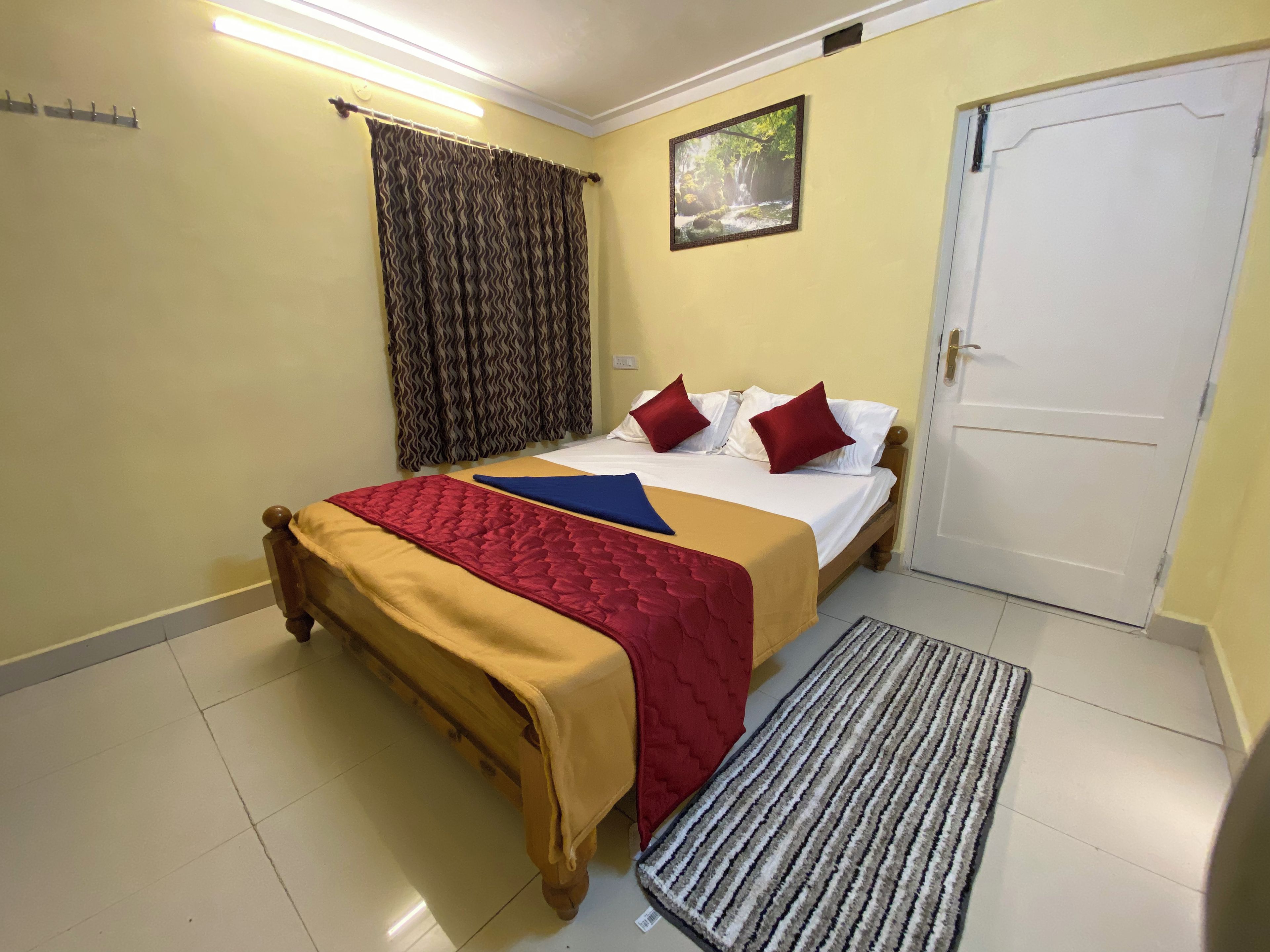 Una habitación de hotel con cama, una puerta, una ventana con cortinas y un cuadro en la pared.