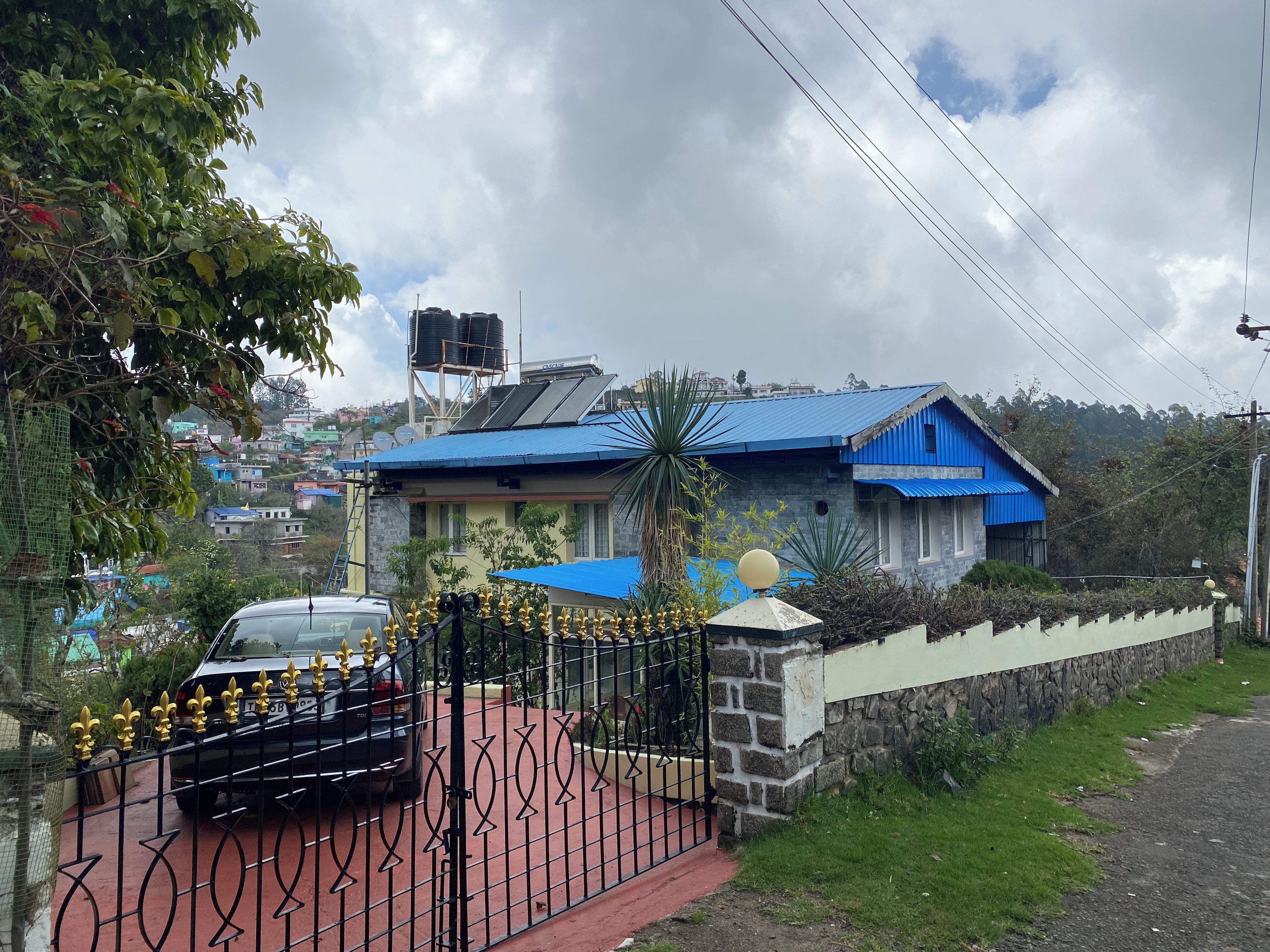 Uma casa com telhado azul, entrada com portão e um carro estacionado.