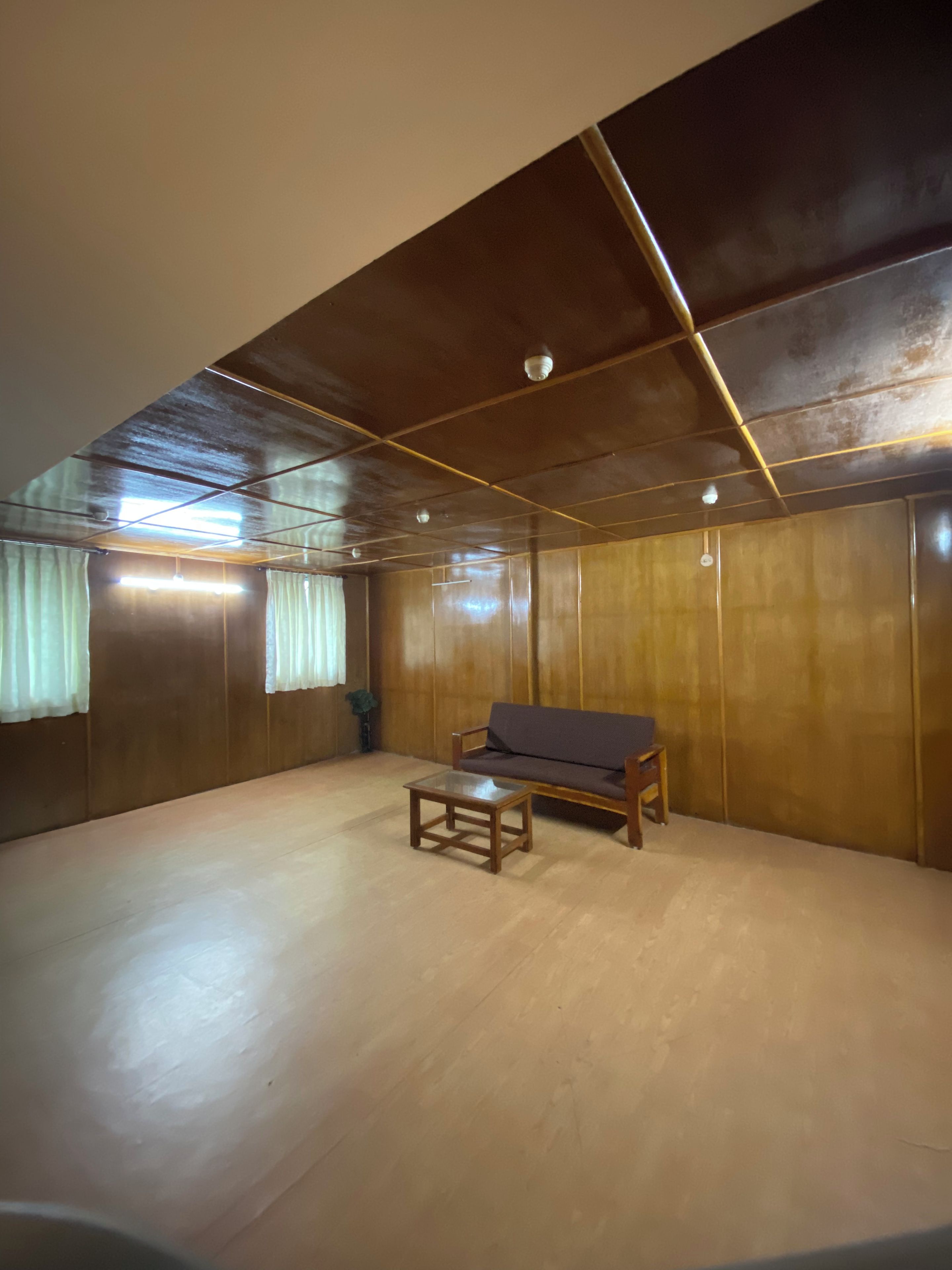 Una habitación con piso de madera, un sofá, una mesita y techo con vigas a la vista e iluminación.