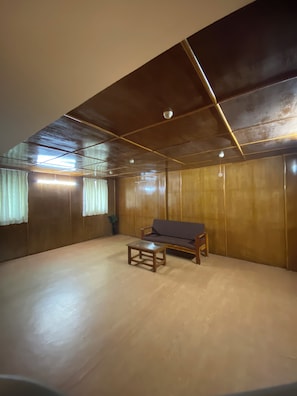 Una habitación con piso de madera, un sofá, una mesita y techo con vigas a la vista e iluminación.