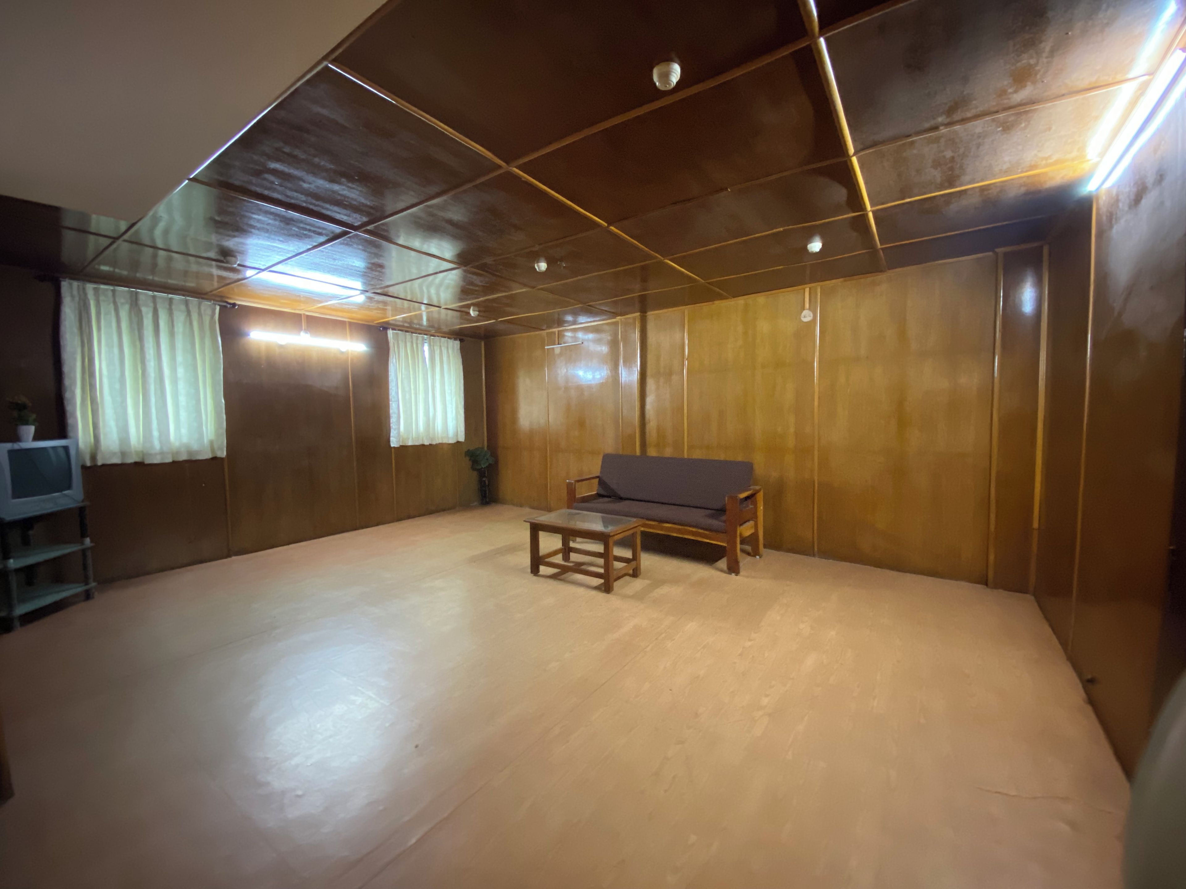 A room with a wooden floor, a sofa, a small table, and a television on a stand.