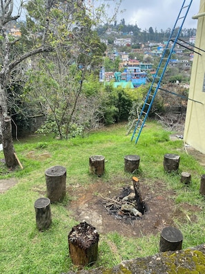 Un espacio al aire libre con césped, troncos de madera, una escalera y una vista de una zona residencial al fondo.