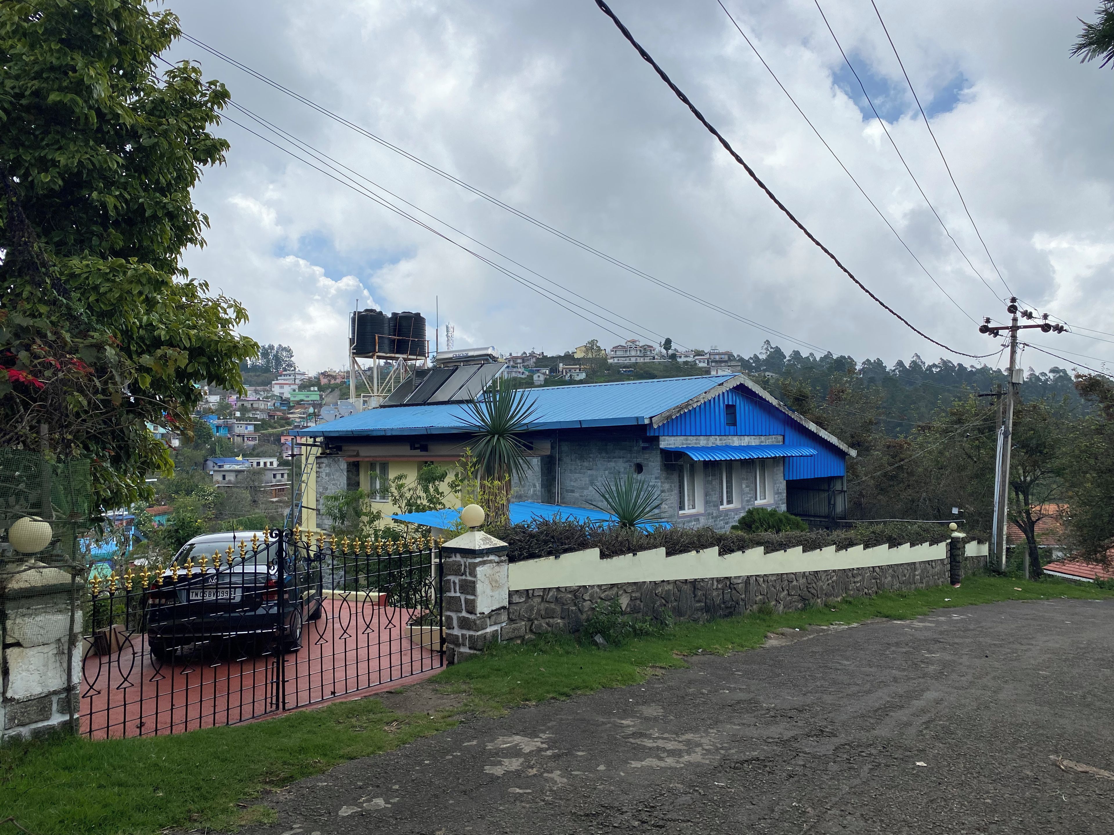 A residential building with a blue roof, a stone wall, and a paved driveway.