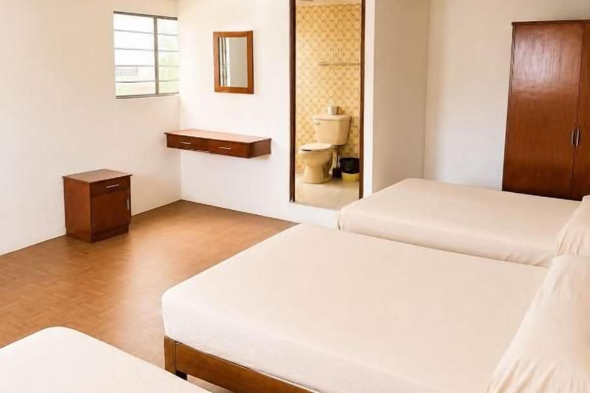 A hotel room with a bed, a wooden cabinet, a small bedside table, and a mirror.
