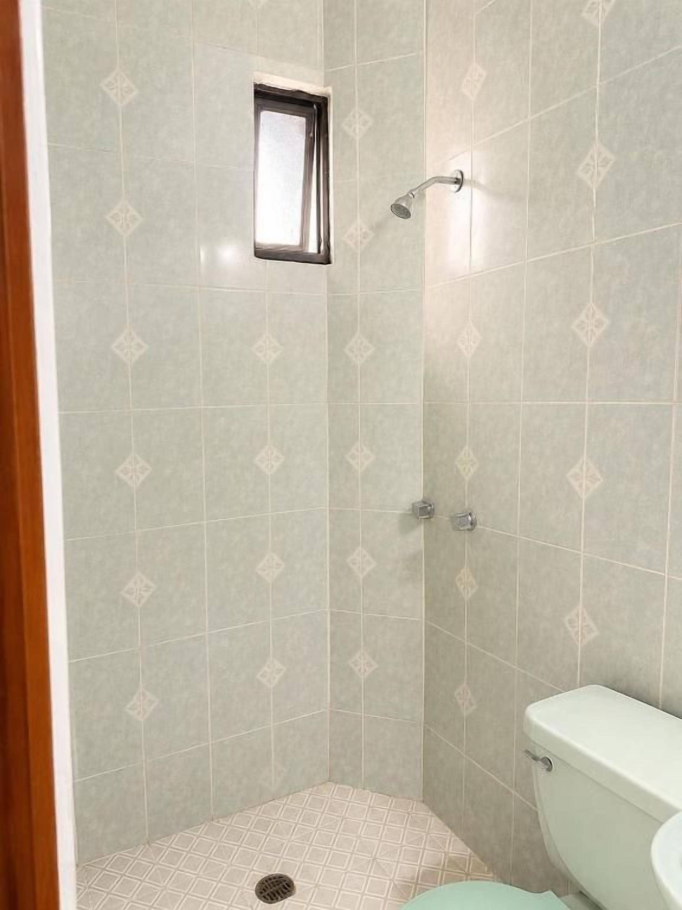 Un área de ducha pequeña y cerrada, con un inodoro a la derecha.