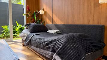 A modern bedroom with a grey sofa bed, a bedside table, and a potted plant.