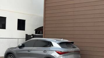 A gray SUV parked in a driveway with a white building and a brown wall in the background.