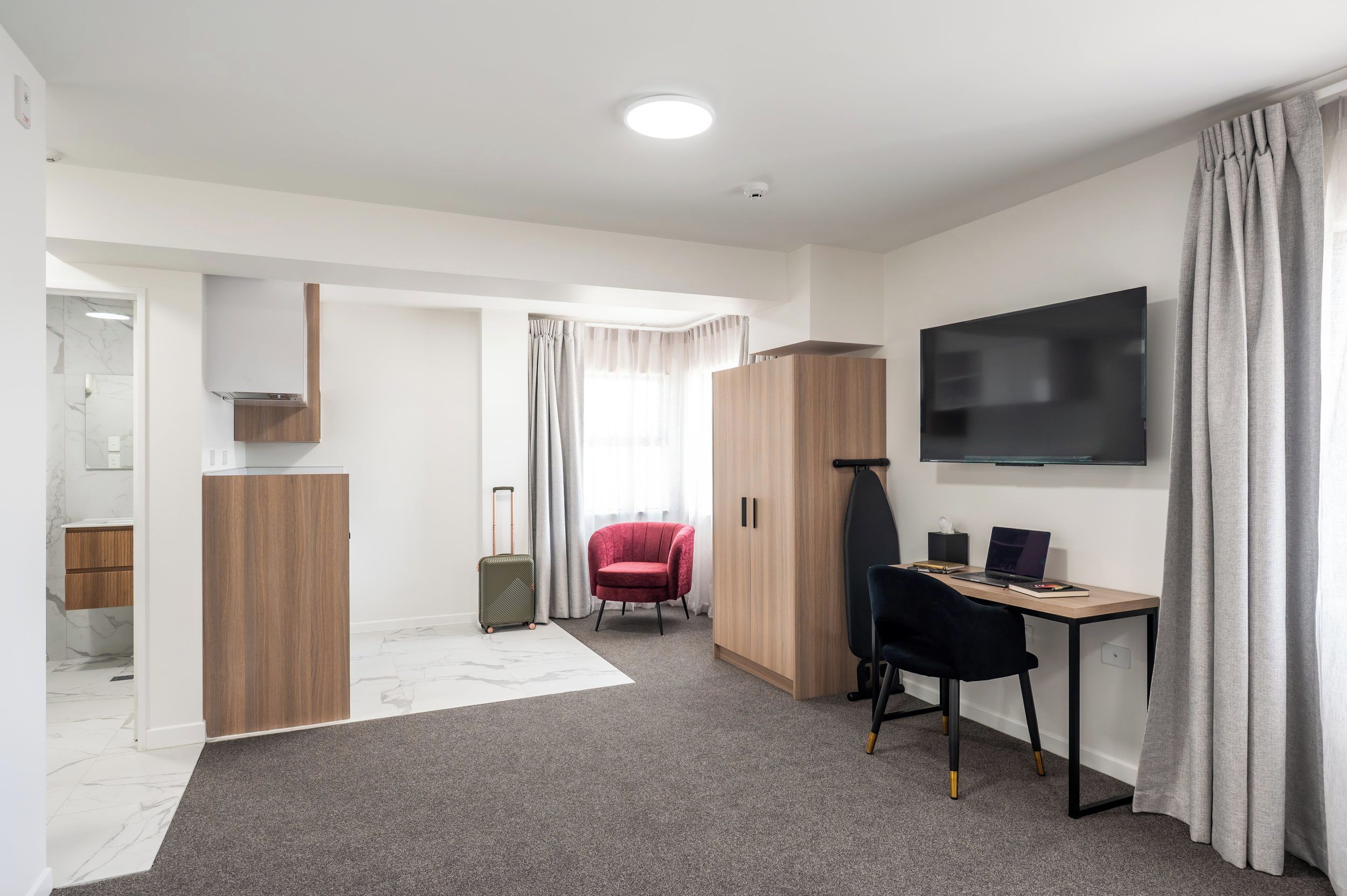Une chambre d’hôtel équipée d’un bureau, d’une chaise, d’une télévision, d’une armoire et d’une salle de bain visible à travers une porte ouverte.