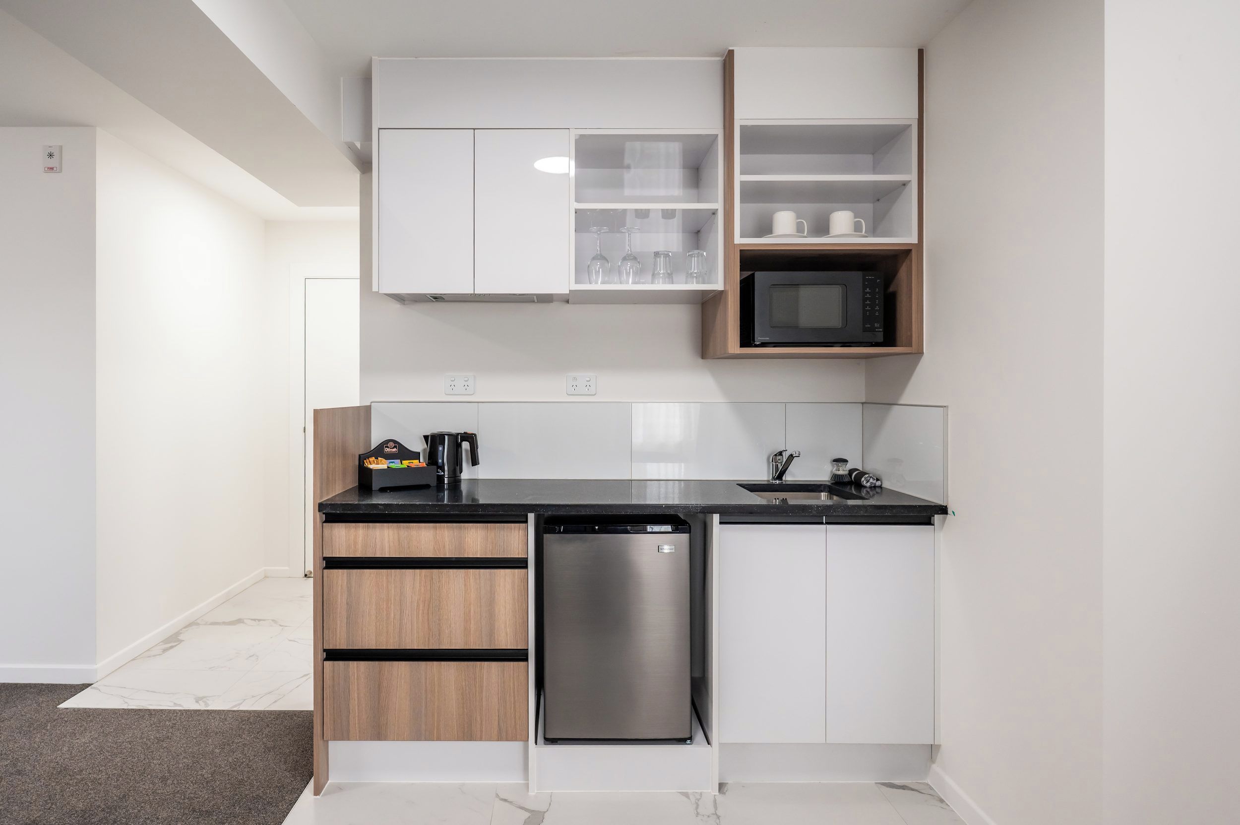Una cocina compacta con armarios blancos, encimera negra, lavavajillas de acero inoxidable y microondas.