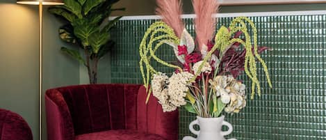 Una sala moderna con un sillón de terciopelo rojo, un jarrón blanco con flores secas, una mesa de centro negra y un libro titulado 'Gucci'.