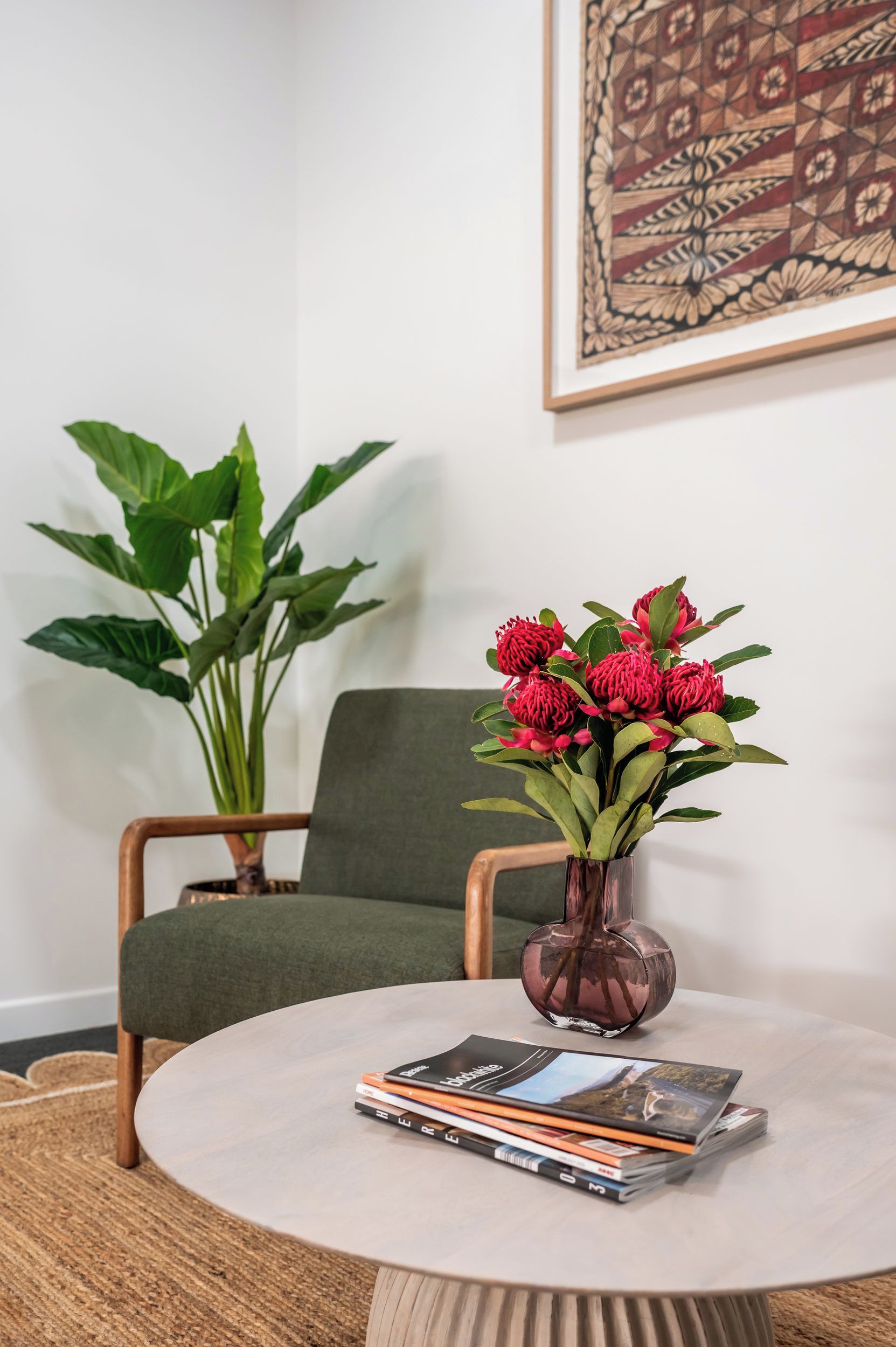 Une pièce avec une table ronde, une chaise verte, une plante en pot et un vase rempli de fleurs rouges.