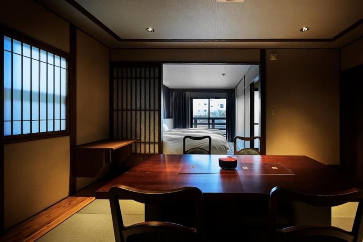 Et traditionelt japansk rum med tatami-gulv, et lavt bord med stole og en skydedør, der fører til en balkon med udsigt.