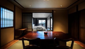 Et traditionelt japansk rum med tatami-gulv, et lavt bord med stole og en skydedør, der fører til en balkon med udsigt.