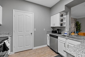 A kitchen with white cabinets, a dishwasher, and a granite countertop. - Stylish 2BR | Pool | Near Universal & Disney (Orlando)