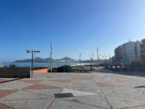 A paved promenade with directional signs, a clear view of the sea, and distant mountains. - GuestReady - Canteras Surf, Relax & Work (Las Palmas de Gran Canaria)