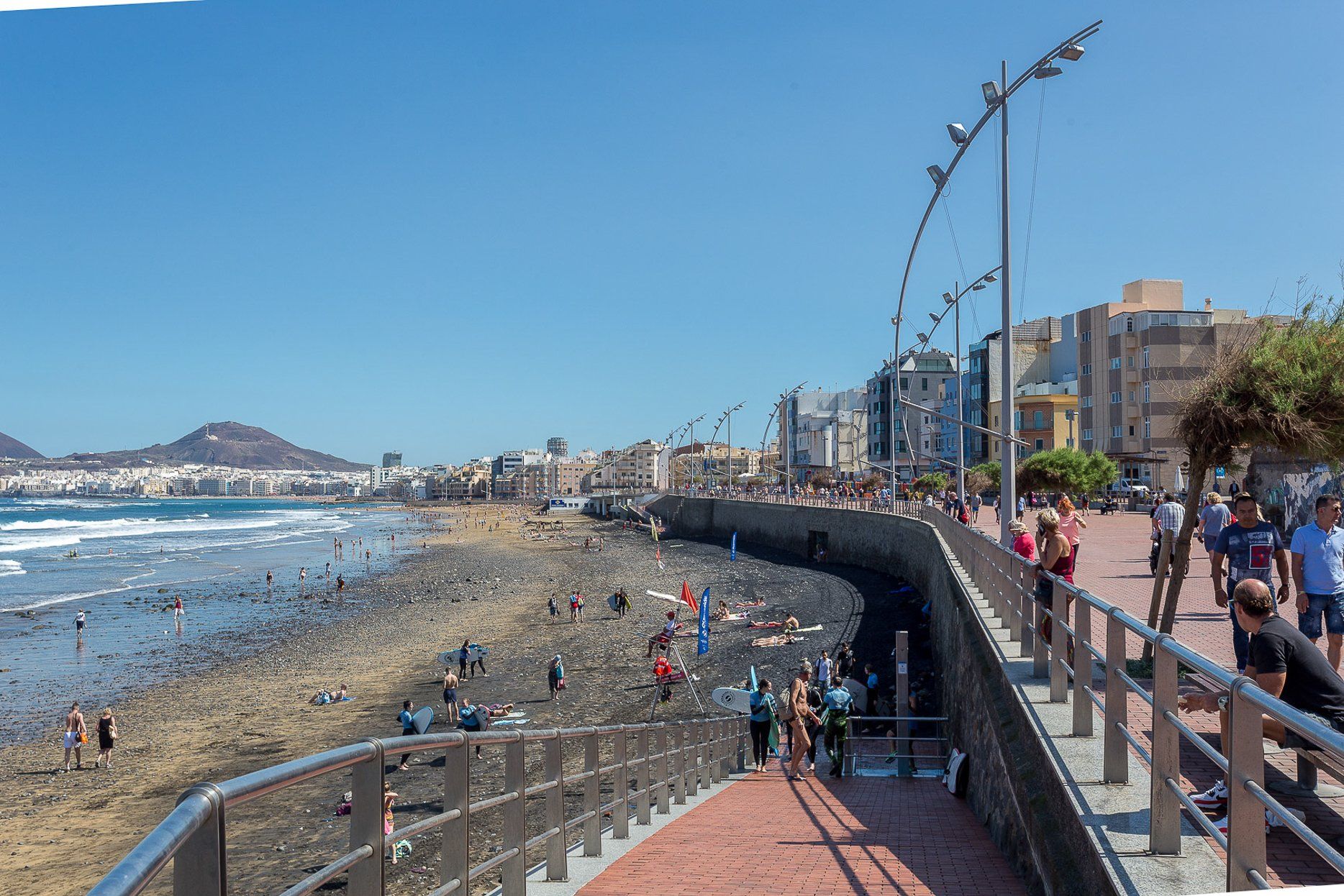 Een kustpromenade met een pad van stenen, een strand en stadsgebouwen op de achtergrond.