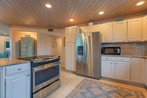 A kitchen with white cabinets, stainless steel appliances, a granite countertop, and a patterned rug. - Sea Cove Castle by Duncan Real Estate (Anna Maria)