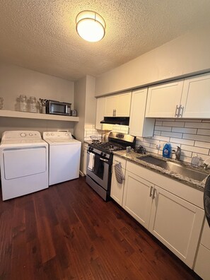 A kitchen with white cabinets, a stove, a microwave, and a washing machine. - Cozy 2-bedroom homeNear Downtown and Speedway (Indianapolis)