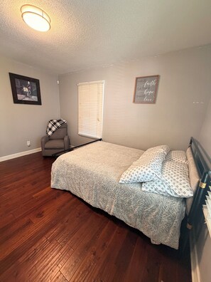 A bedroom with a bed, a chair, a window with blinds, and a ceiling light fixture. - Cozy 2-bedroom homeNear Downtown and Speedway (Indianapolis)