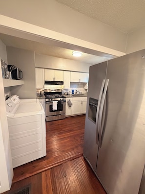 A compact kitchen with white cabinets, a stainless steel refrigerator, a built-in oven, and a microwave. - Cozy 2-bedroom homeNear Downtown and Speedway (Indianapolis)