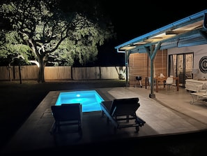 A backyard with a swimming pool, lounge chairs, a barbecue, and a covered patio area.