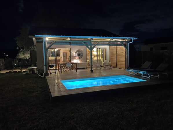 A modern outdoor pool area with a covered patio and lounge chairs.