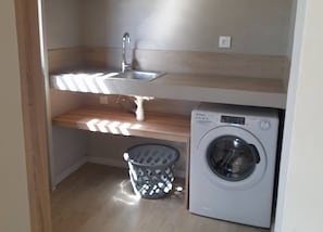 A compact laundry area with a washing machine, a sink, and a laundry basket.