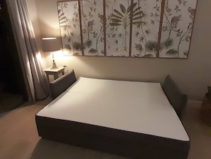 A bedroom with a bed, a nightstand, a lamp, and a wall with a nature-themed artwork.