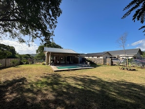 A residential property with a covered outdoor seating area, a swimming pool, and a stone wall.
