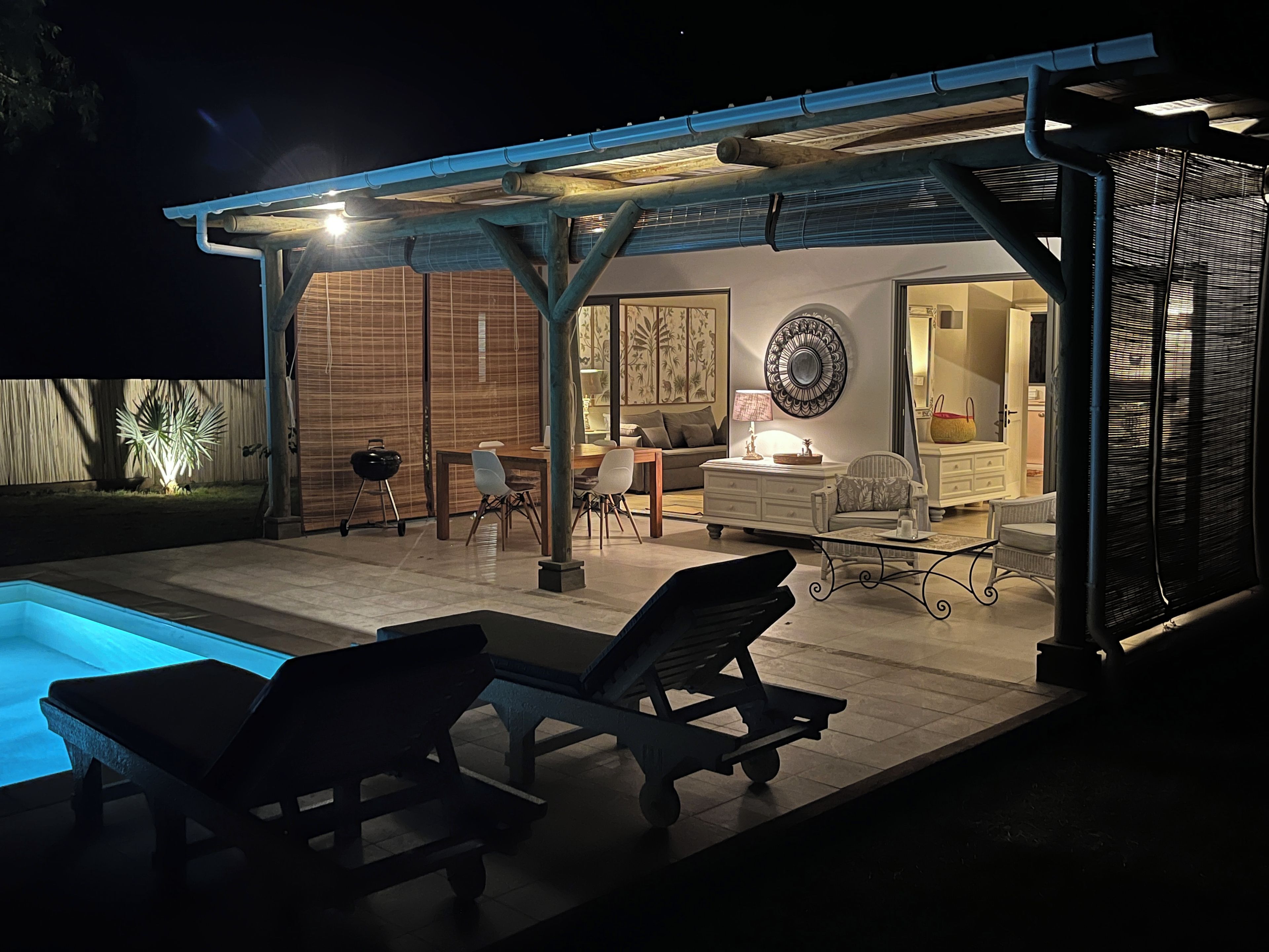A covered outdoor area with a pool, lounge chairs, a dining table, and a living room setup.