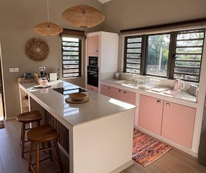 A modern kitchen with a central island, bar stools, a large window, and a patterned rug.