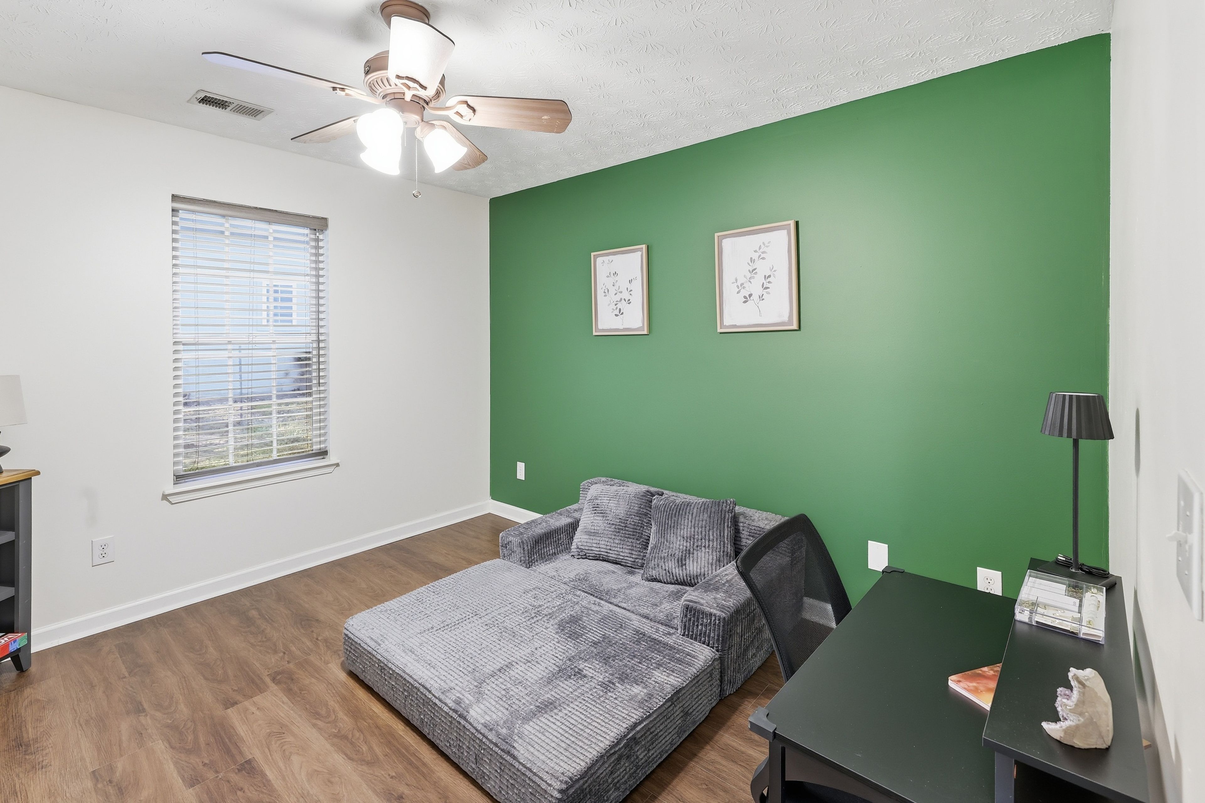 A room with a bed, a desk, a lamp, and two framed pictures on the wall.
