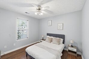 Une chambre à coucher avec un lit, des tables de chevet, un ventilateur de plafond et une fenêtre.