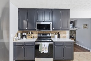 Une cuisine avec des meubles de couleur gris foncé, un four à micro-ondes en acier inoxydable et un four Samsung.