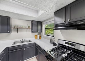 A modern kitchen with dark cabinetry, a stainless steel sink, and a gas stove. - Near Zoo•Private Balcony•3 TVS (San Antonio)