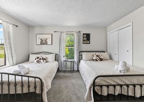 A twin bedroom with two beds, a window with curtains, a wall-mounted picture, and a door. - Near Zoo•Private Balcony•3 TVS (San Antonio)