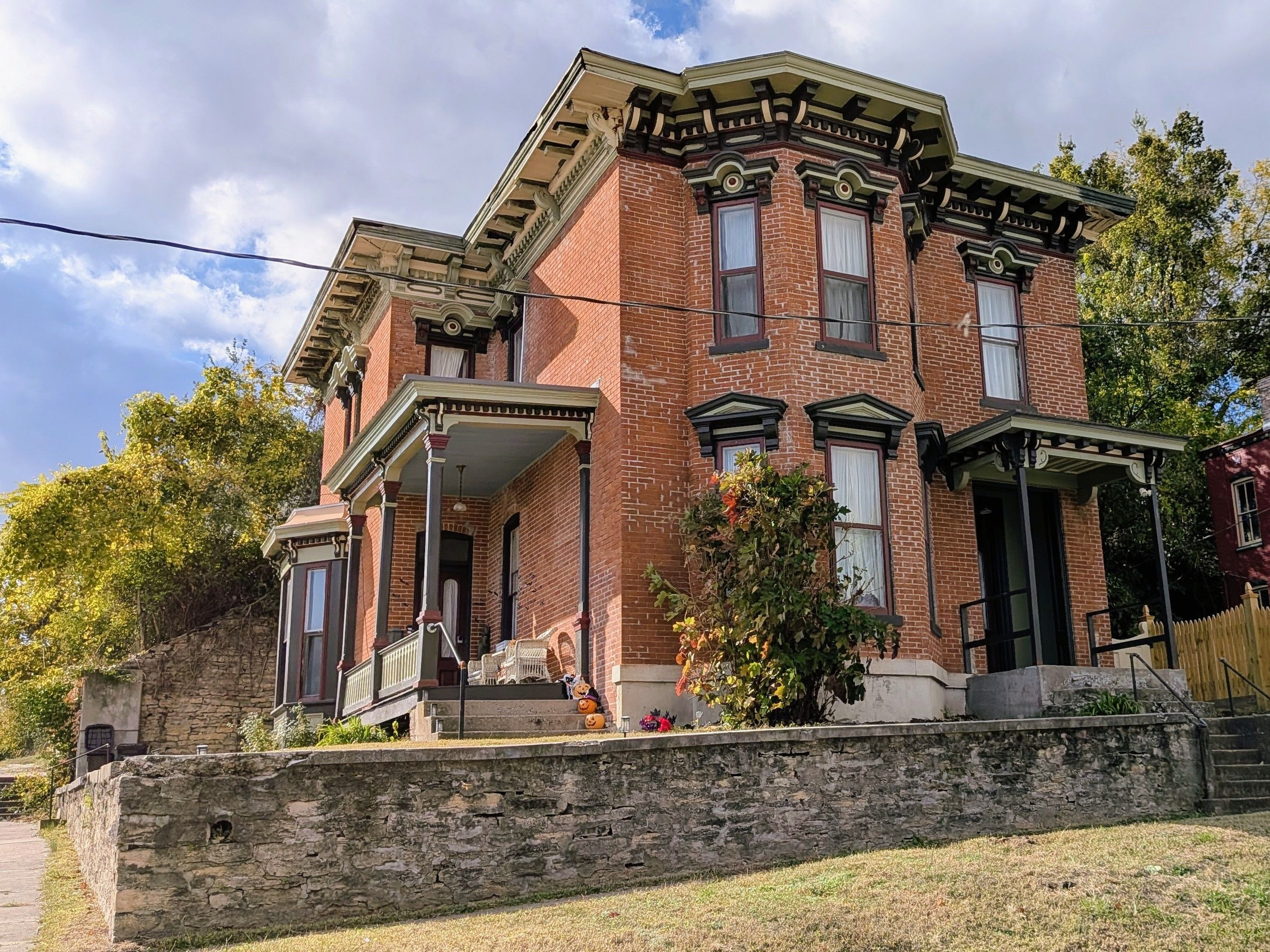 A two-story brick building with a porch, a stone retaining wall, and a small garden with a pumpkin decoration.