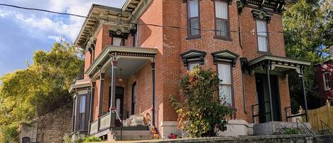 A two-story brick building with a porch, a stone retaining wall, and a small garden with a pumpkin decoration.