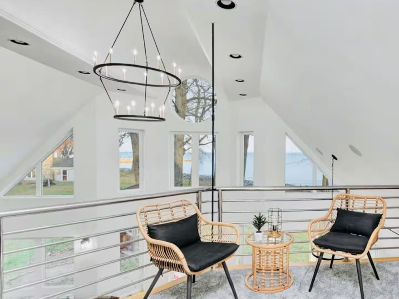 En modern inredning med två fåtöljer i rotting, ett litet bord och ett stort fönster med utsikt över omgivningen.